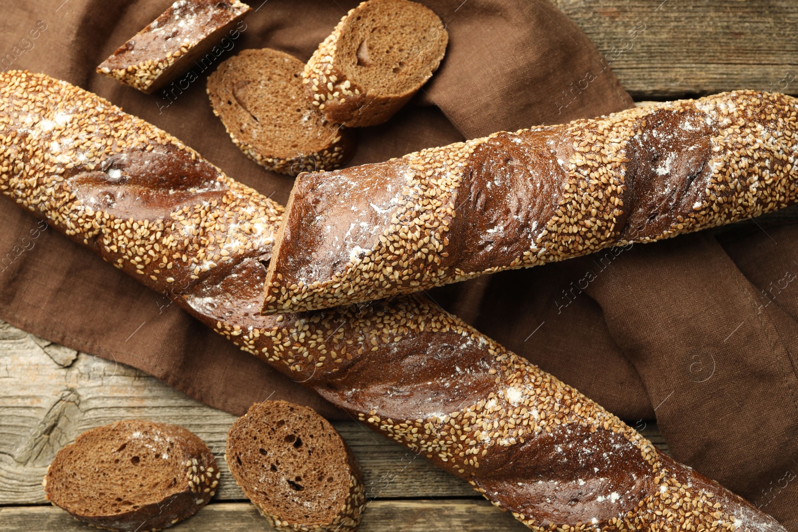 Photo of Fresh baguettes with sesame on wooden table, flat lay