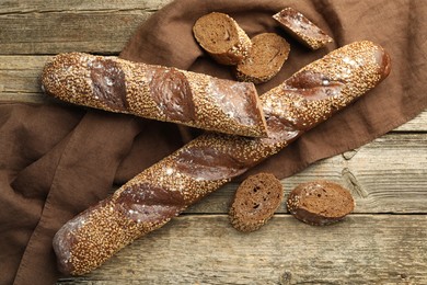 Photo of Fresh baguettes with sesame on wooden table, flat lay