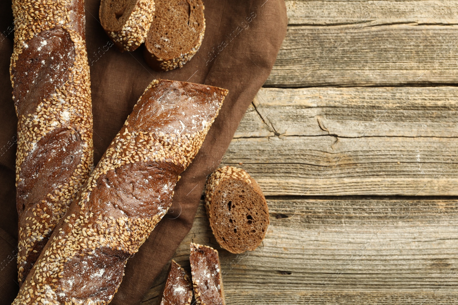 Photo of Fresh baguettes with sesame on wooden table, flat lay. Space for text