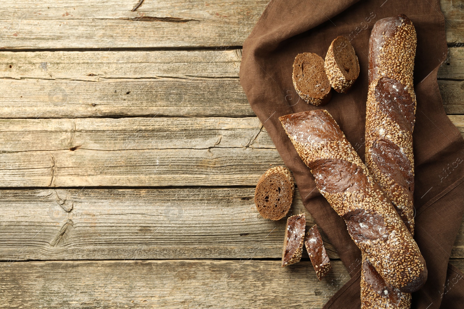 Photo of Fresh baguettes with sesame on wooden table, flat lay. Space for text