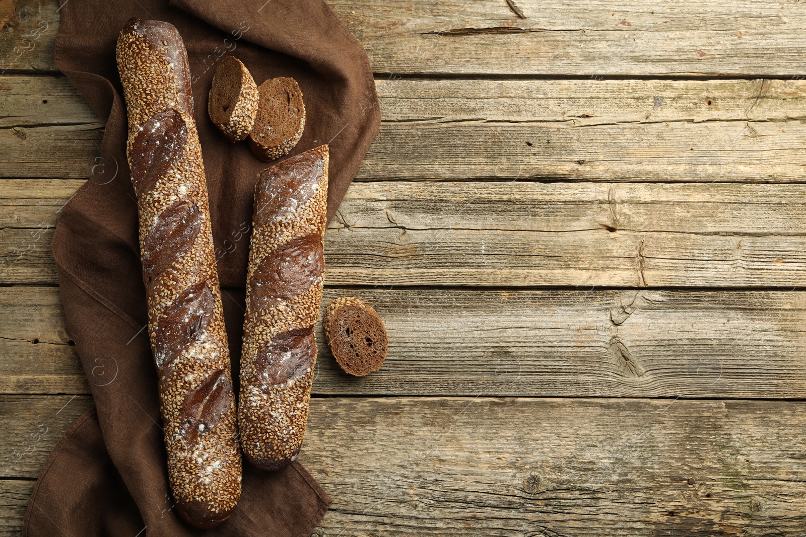 Photo of Fresh baguettes with sesame on wooden table, flat lay. Space for text