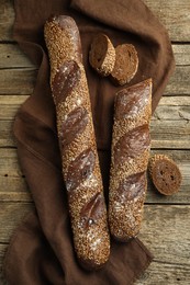 Photo of Fresh baguettes with sesame on wooden table, flat lay