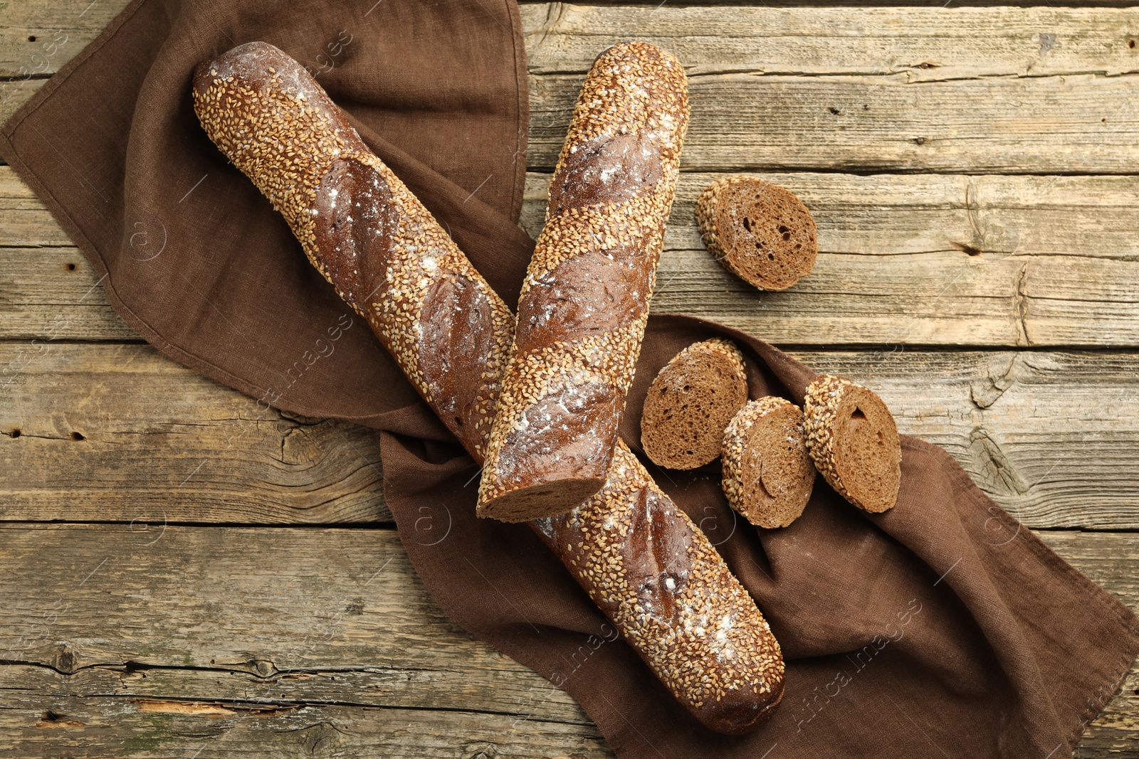 Photo of Fresh baguettes with sesame on wooden table, flat lay