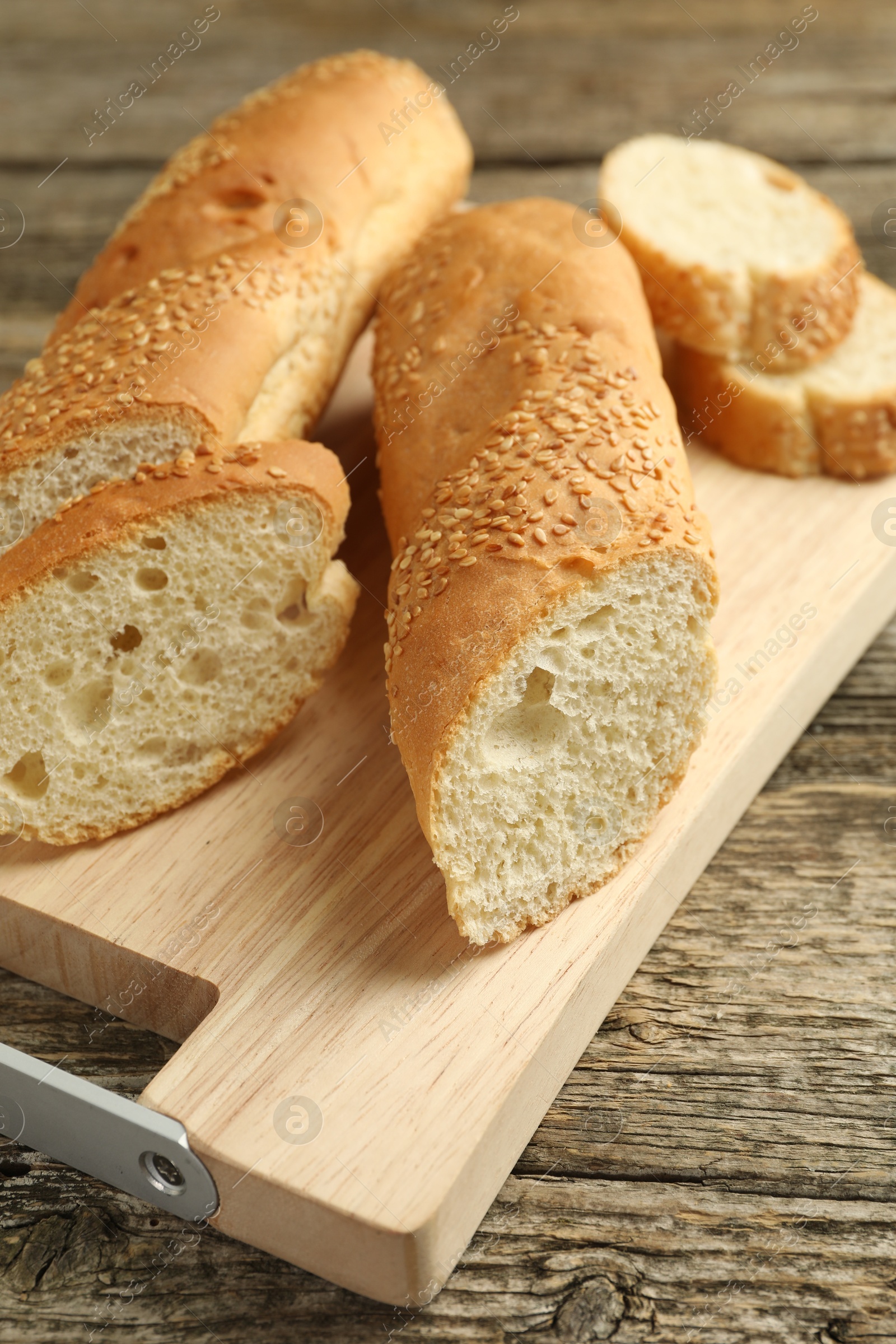 Photo of Cut fresh baguette with sesame on wooden table, closeup