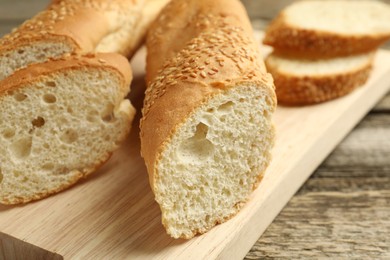 Photo of Cut fresh baguette with sesame on wooden table, closeup