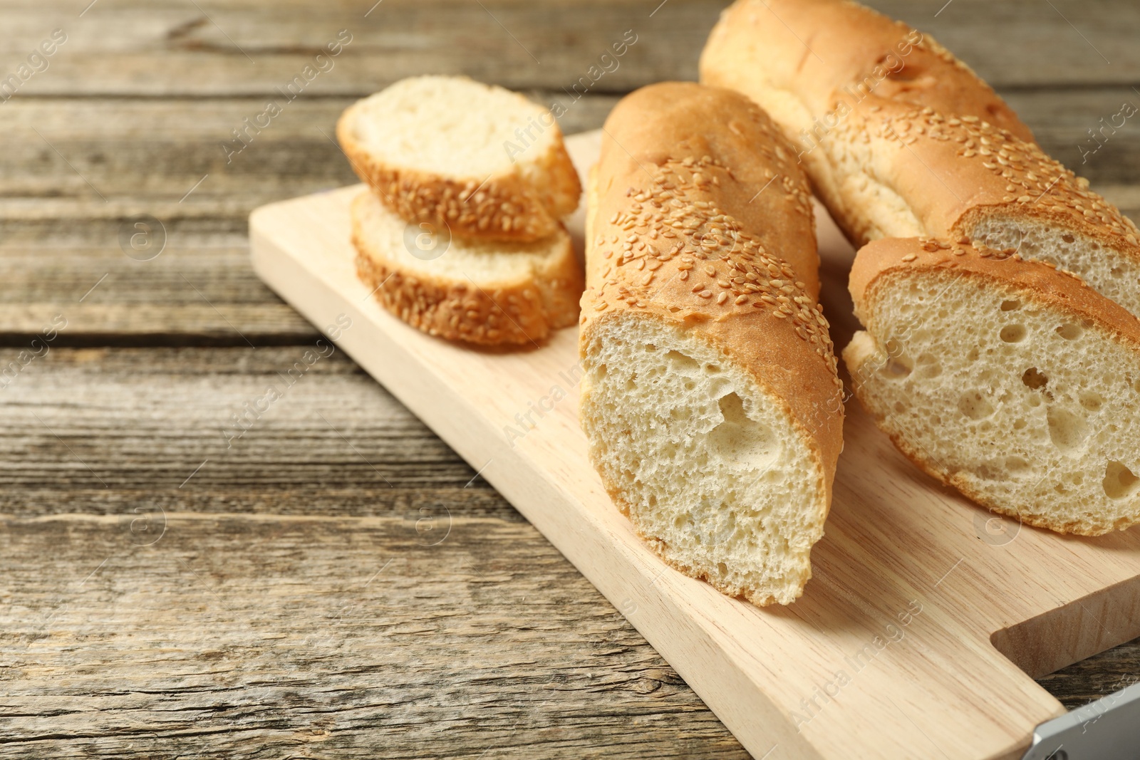 Photo of Cut fresh baguette with sesame on wooden table, closeup. Space for text