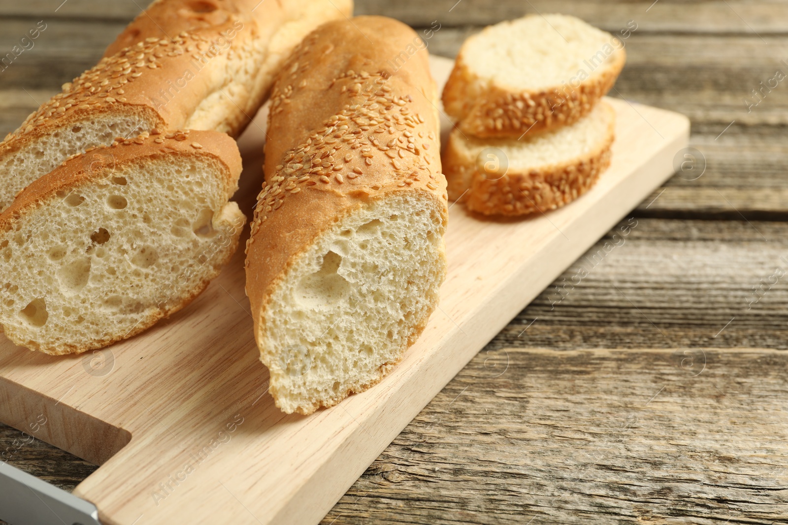 Photo of Cut fresh baguette with sesame on wooden table, closeup. Space for text