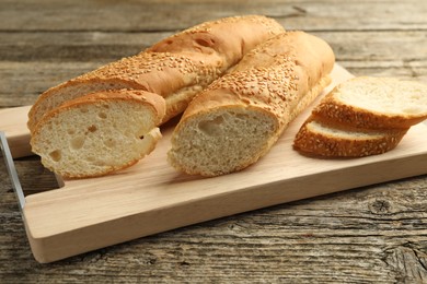 Photo of Cut fresh baguette with sesame on wooden table, closeup