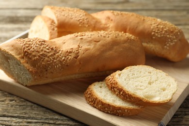 Photo of Cut fresh baguette with sesame on wooden table, closeup