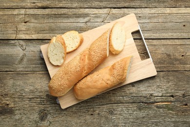 Cut fresh baguette with sesame on wooden table, top view