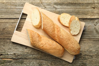 Photo of Cut fresh baguette with sesame on wooden table, top view