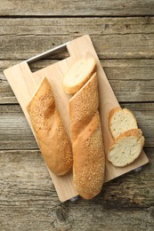 Photo of Cut fresh baguette with sesame on wooden table, top view