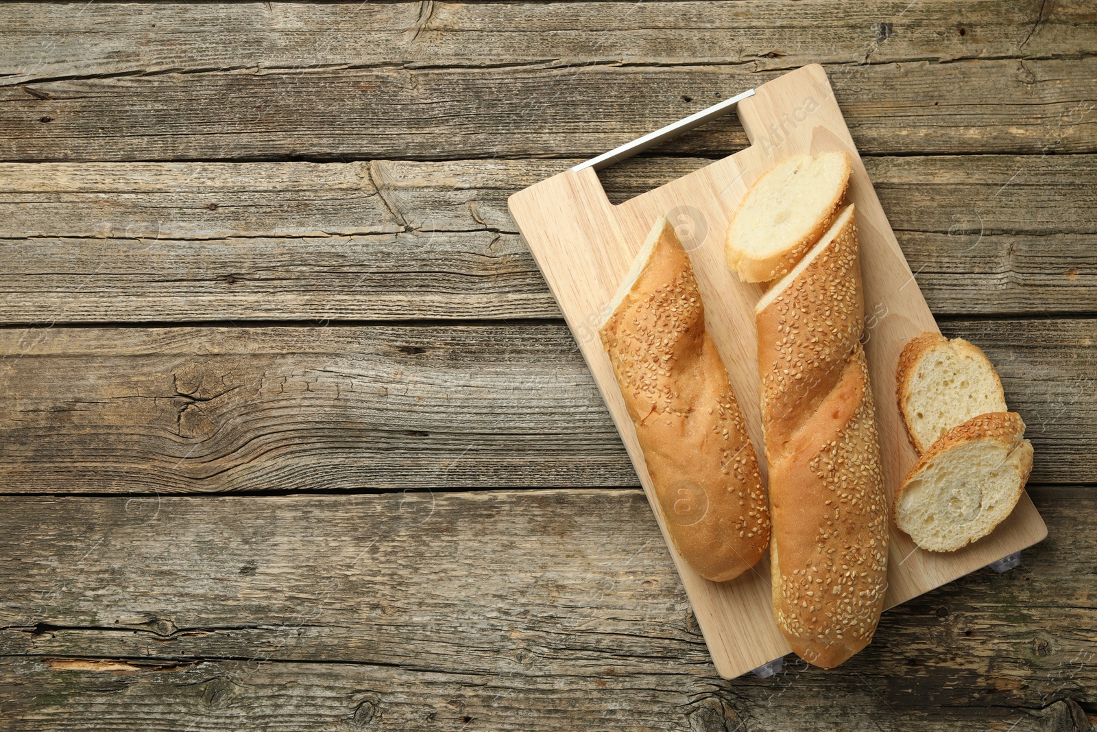 Photo of Cut fresh baguette with sesame on wooden table, top view. Space for text