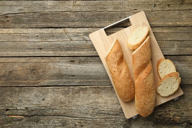 Photo of Cut fresh baguette with sesame on wooden table, top view. Space for text