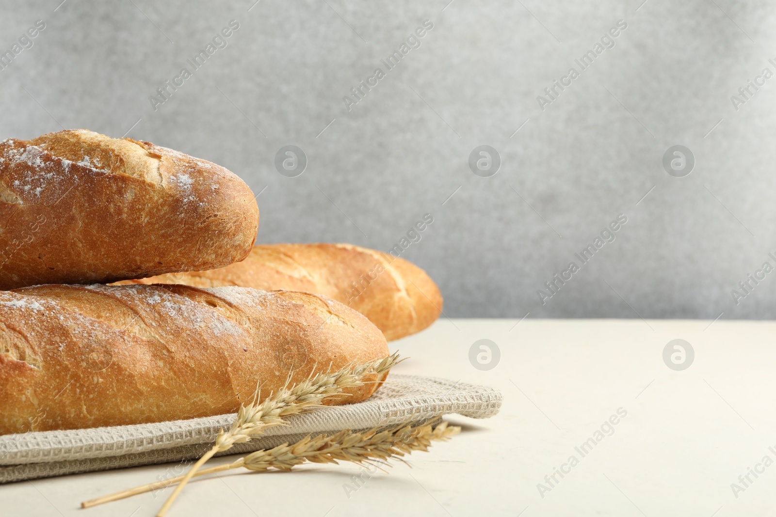 Photo of Fresh baguettes and spikes on beige table, closeup. Space for text