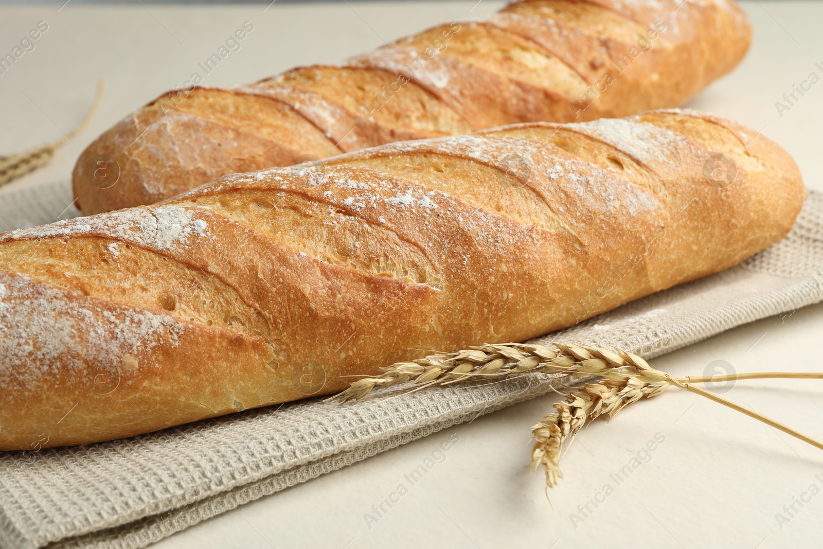 Photo of Fresh baguettes and spikes on beige table, closeup