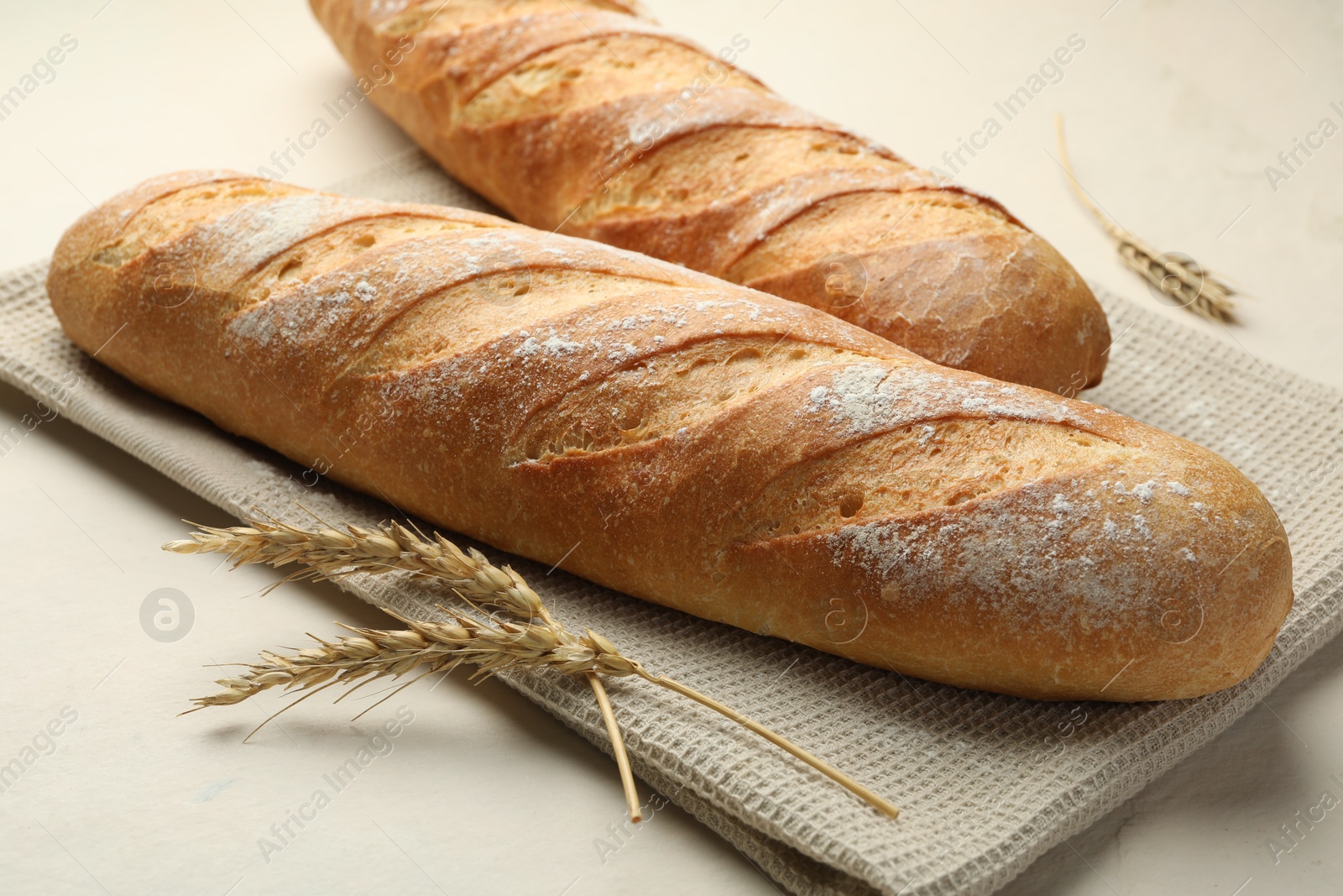 Photo of Fresh baguettes and spikes on beige table, closeup