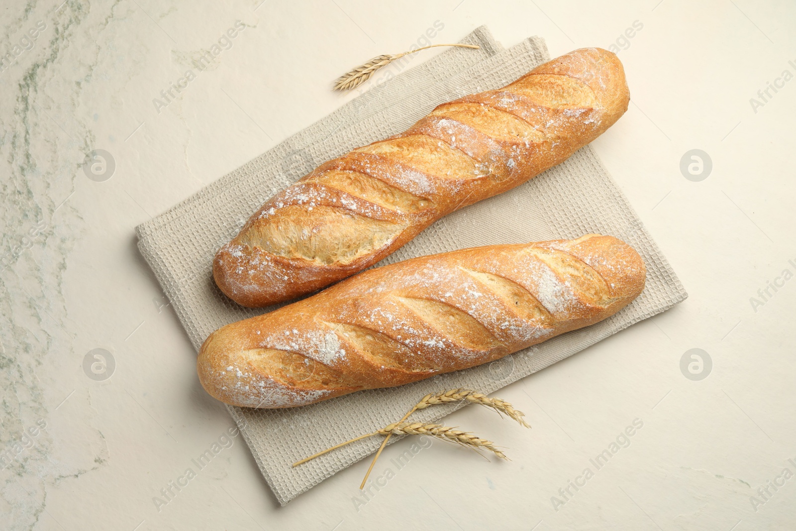 Photo of Fresh baguettes and spikes on beige textured table, flat lay