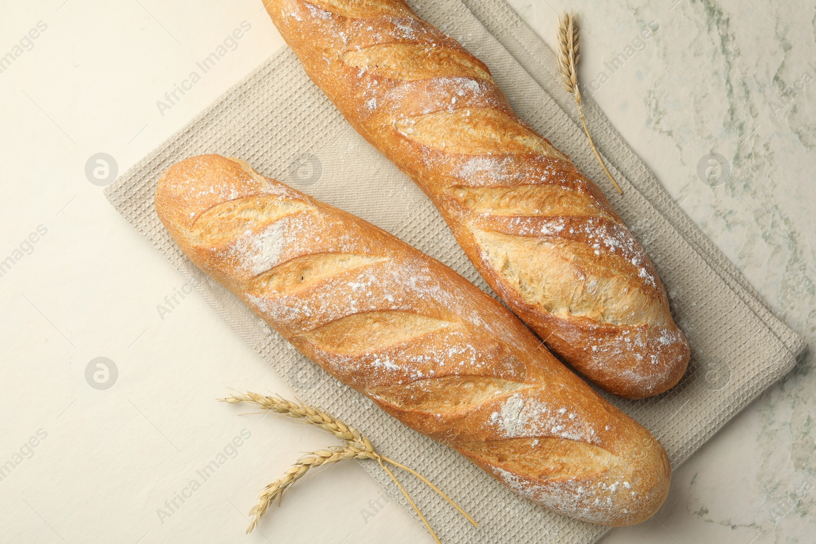 Photo of Fresh baguettes and spikes on beige textured table, flat lay