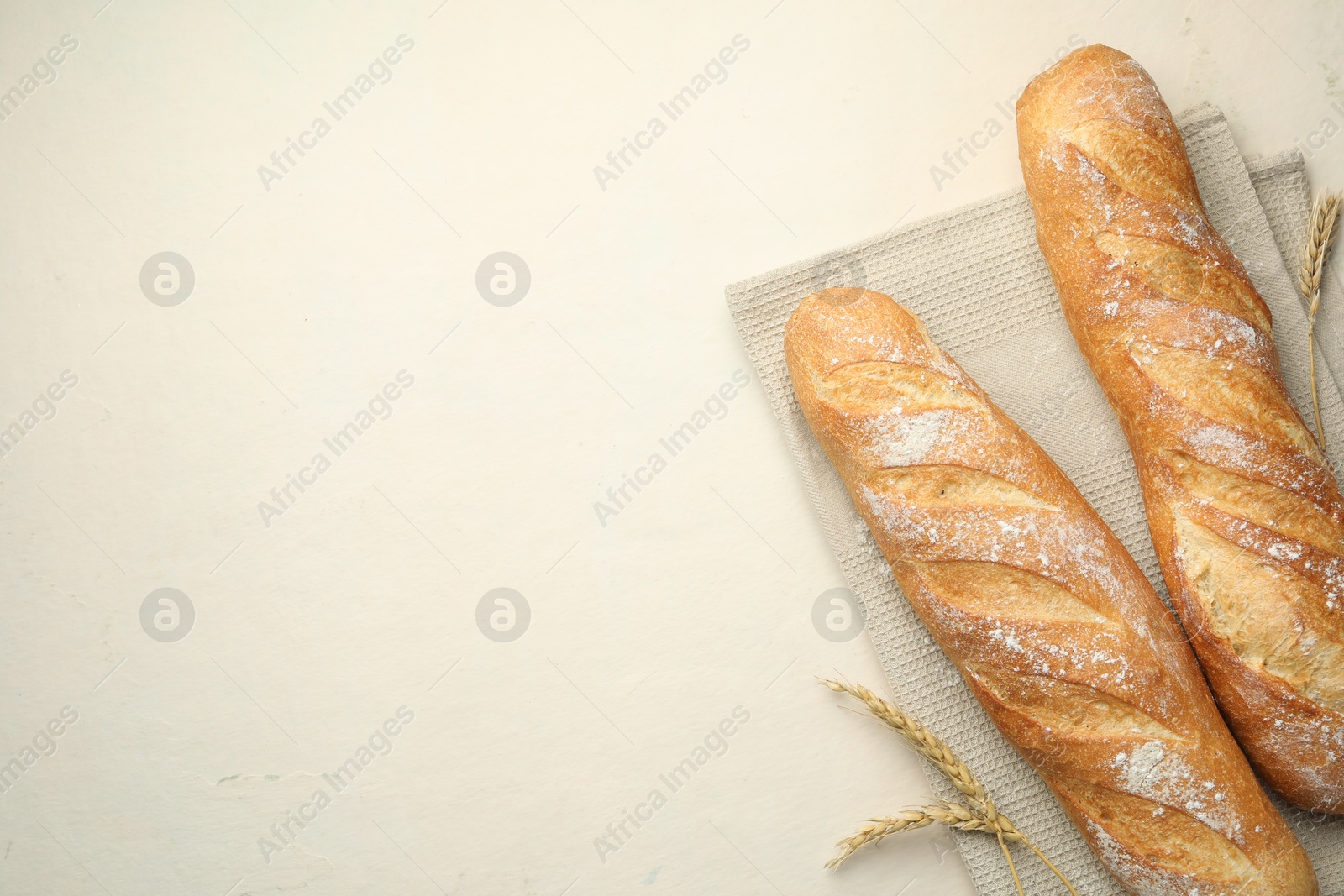 Photo of Fresh baguettes and spikes on beige table, flat lay. Space for text