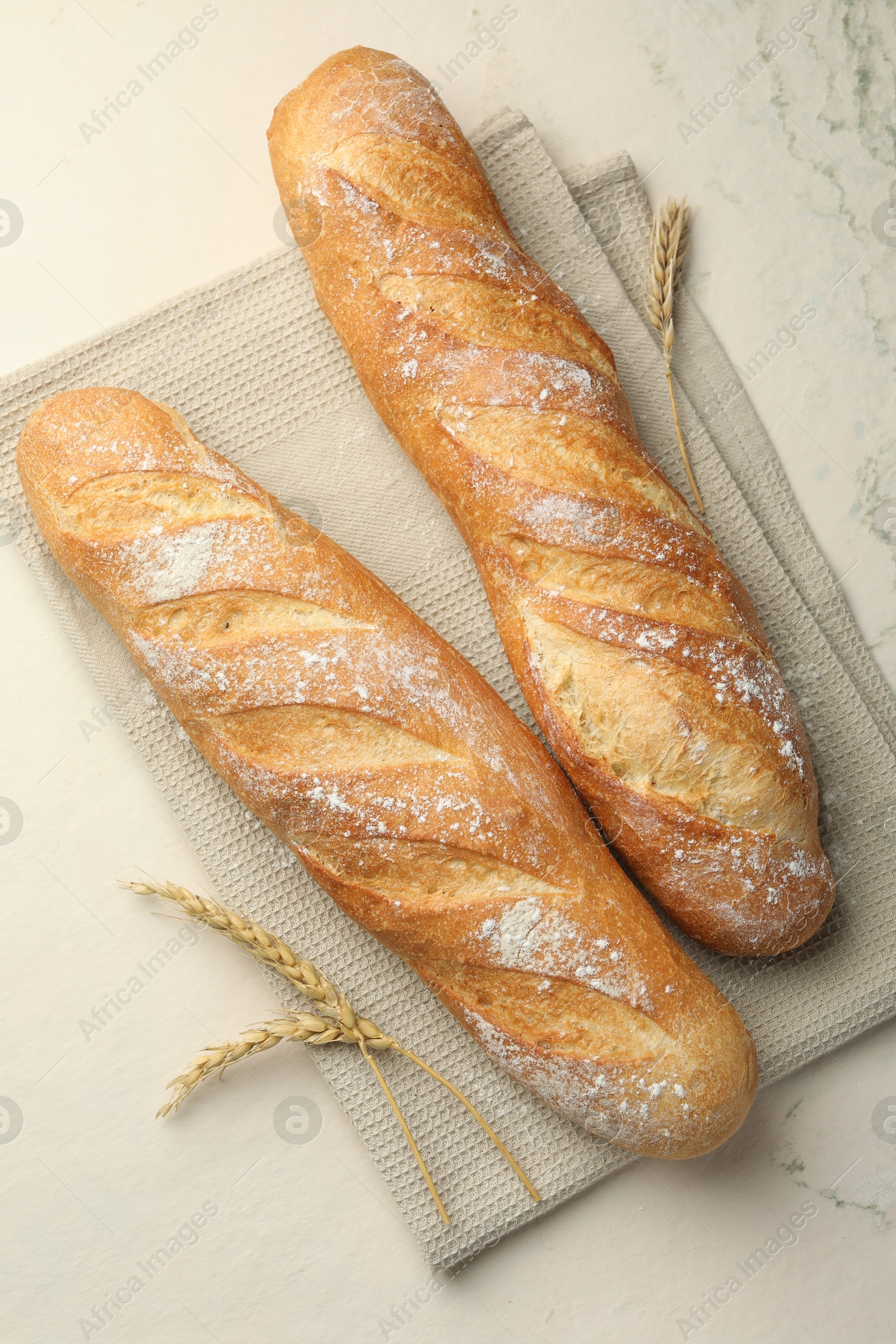 Photo of Fresh baguettes and spikes on beige textured table, flat lay