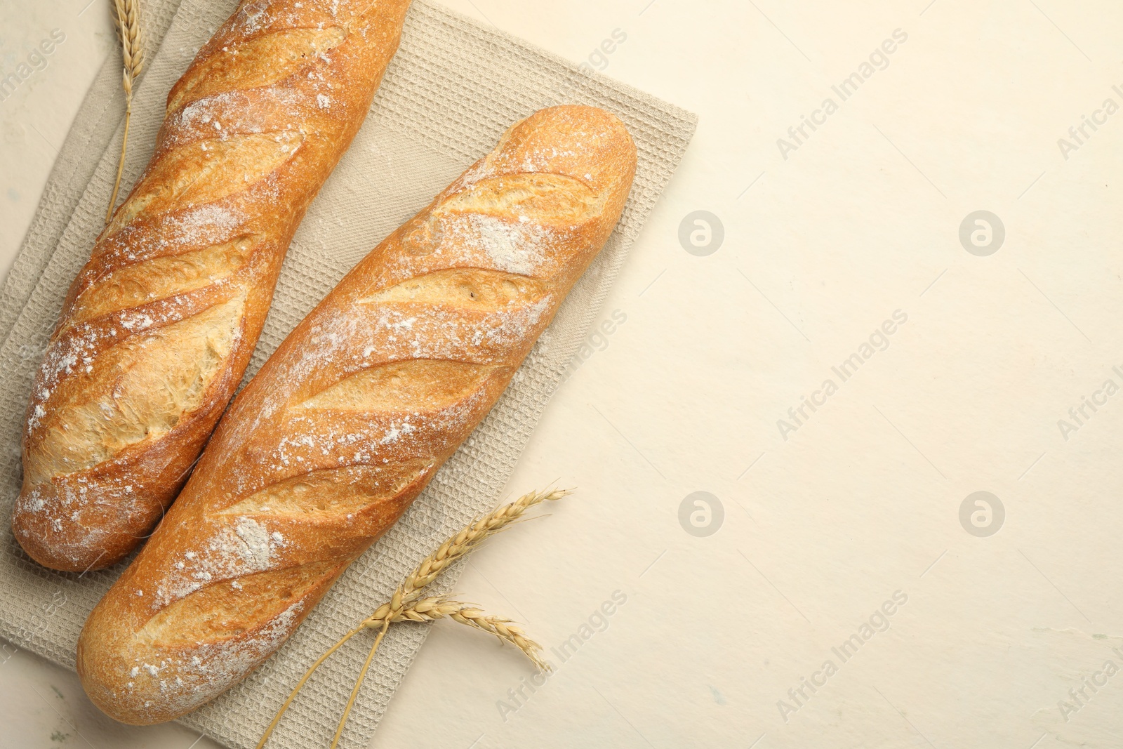 Photo of Fresh baguettes and spikes on beige table, flat lay. Space for text