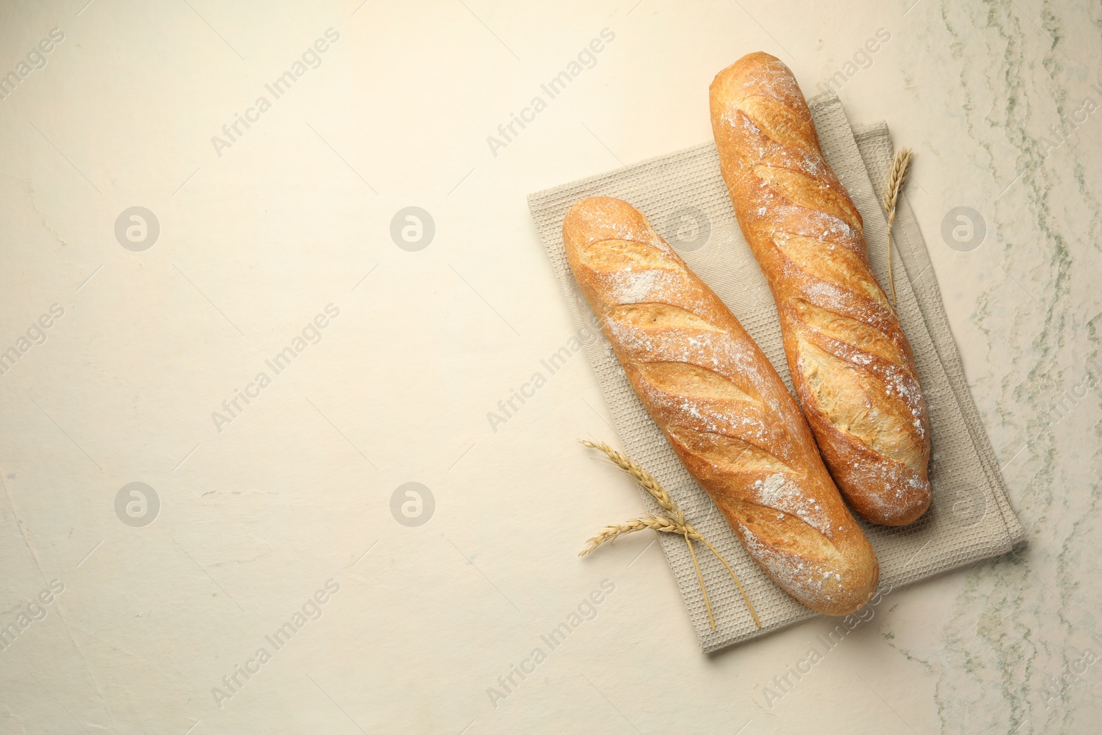 Photo of Fresh baguettes and spikes on beige textured table, flat lay. Space for text