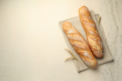 Photo of Fresh baguettes and spikes on beige textured table, flat lay. Space for text