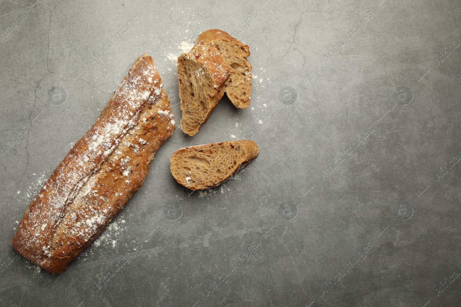 Photo of Cut fresh baguette on grey table, flat lay. Space for text