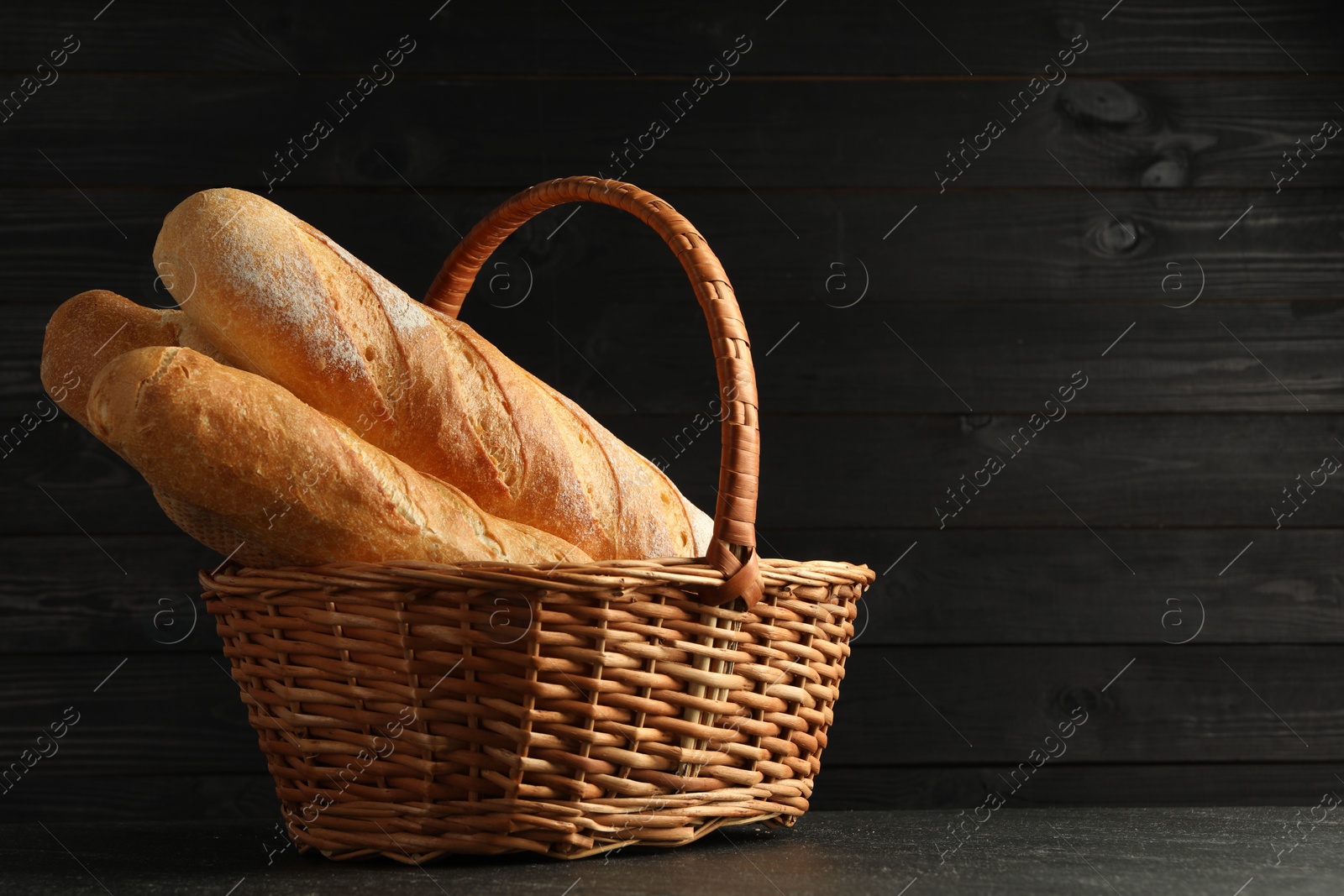 Photo of Fresh baguettes in wicker basket on black table, space for text