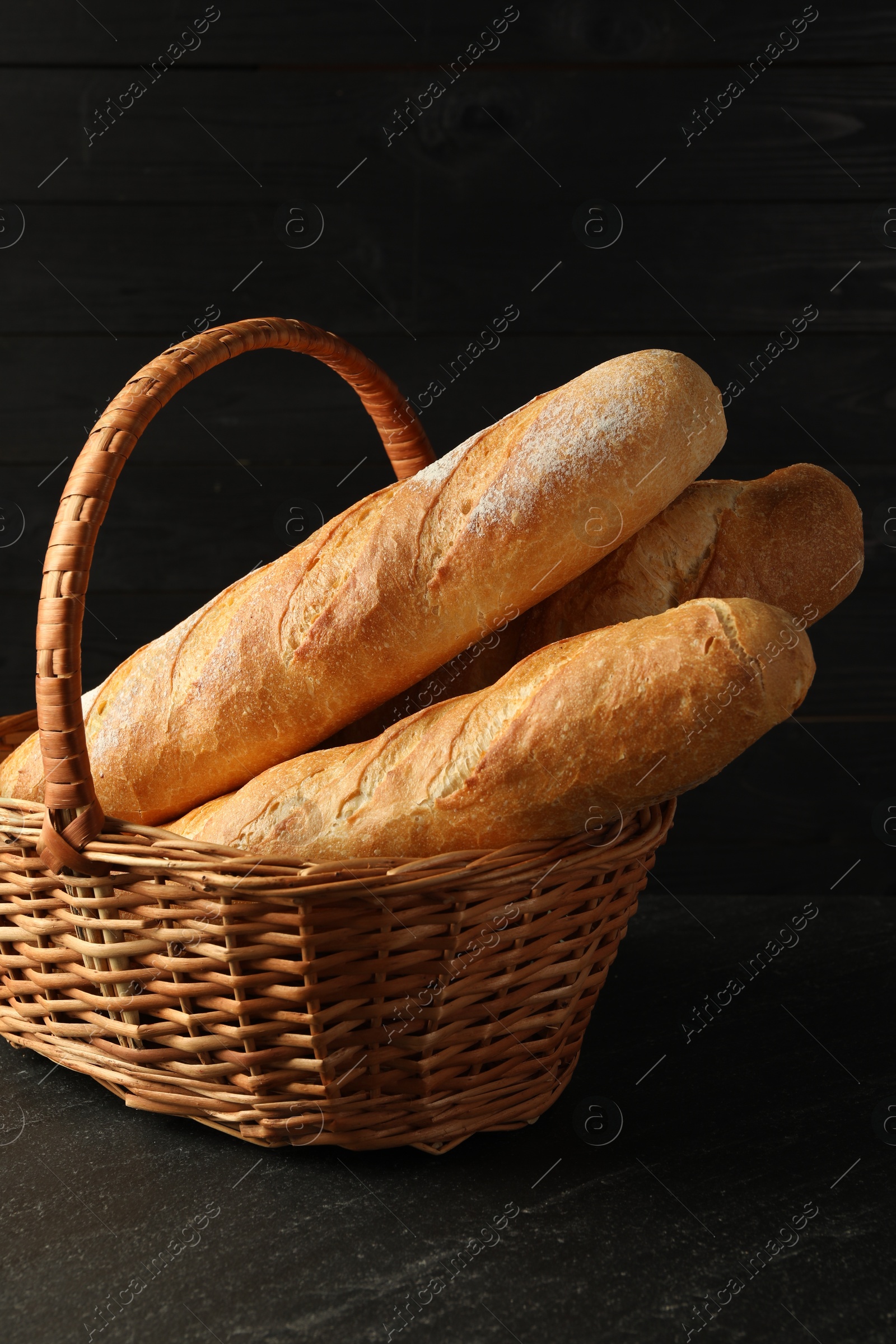 Photo of Fresh baguettes in wicker basket on black table