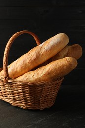 Photo of Fresh baguettes in wicker basket on black table