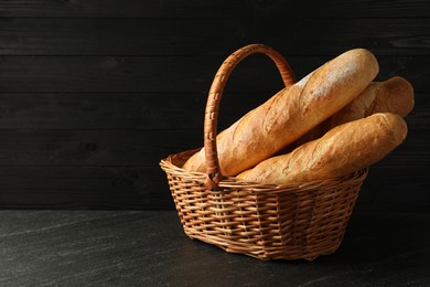 Photo of Fresh baguettes in wicker basket on black table, space for text