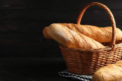 Photo of Wicker basket with fresh baguettes on black table, space for text