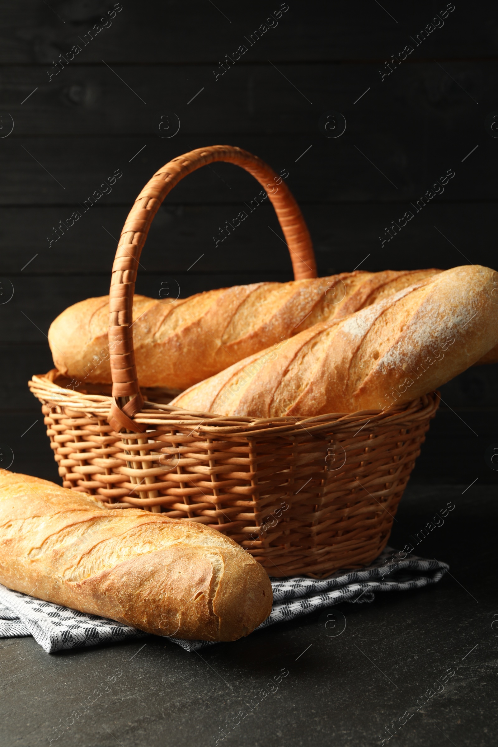 Photo of Wicker basket with fresh baguettes on black table