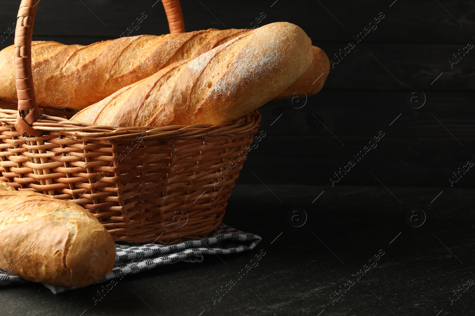 Photo of Wicker basket with fresh baguettes on black table, space for text