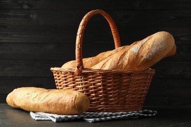 Photo of Wicker basket with fresh baguettes on black table