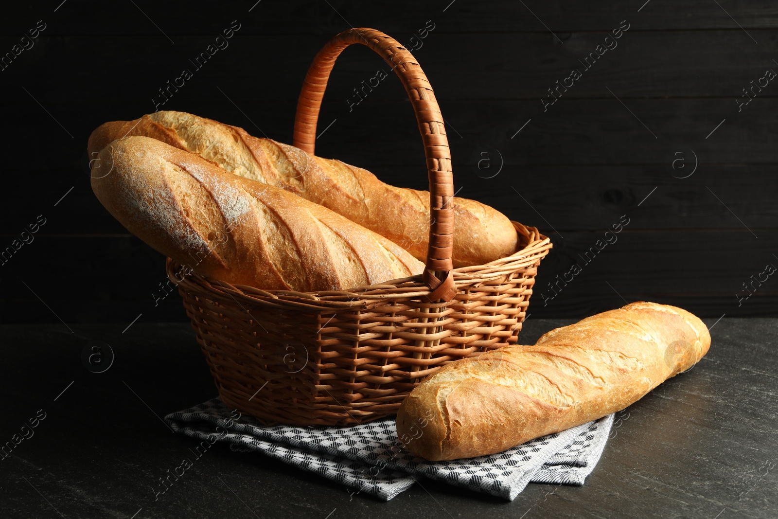 Photo of Wicker basket with fresh baguettes on black table