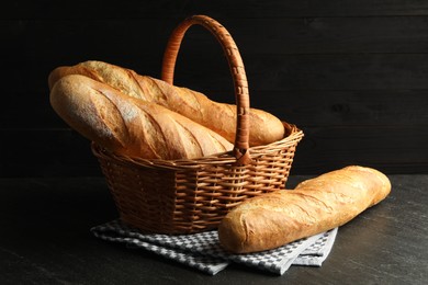 Photo of Wicker basket with fresh baguettes on black table