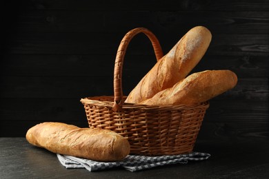 Photo of Wicker basket with fresh baguettes on black table