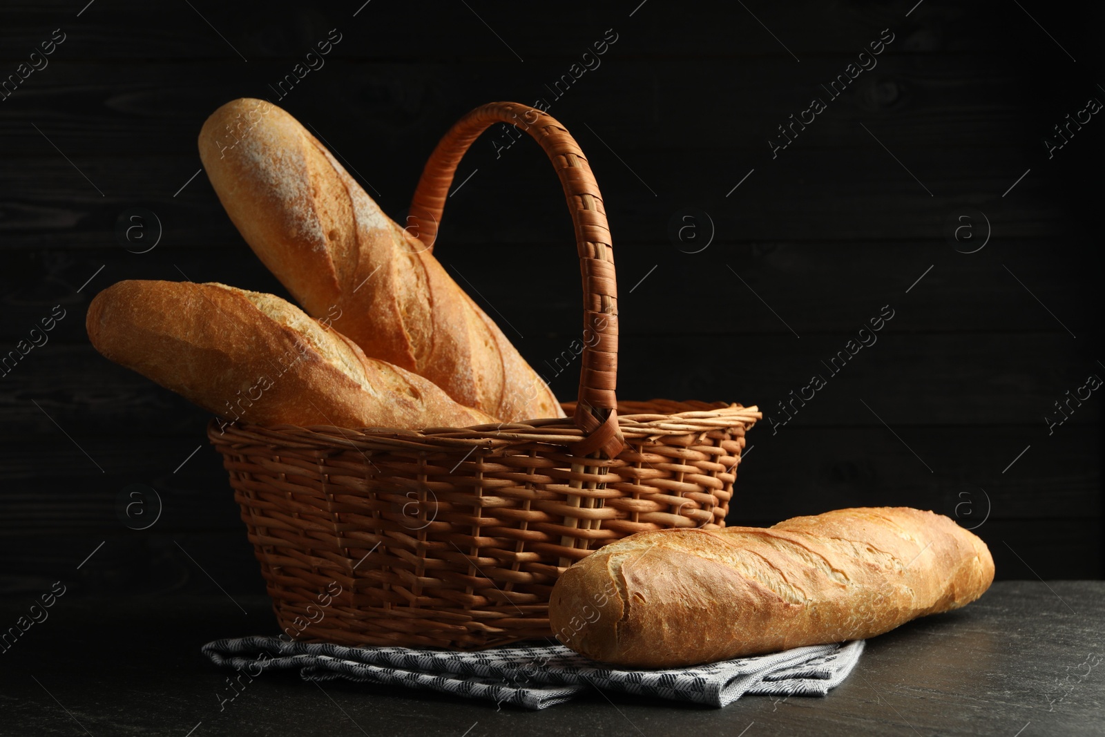 Photo of Wicker basket with fresh baguettes on black table