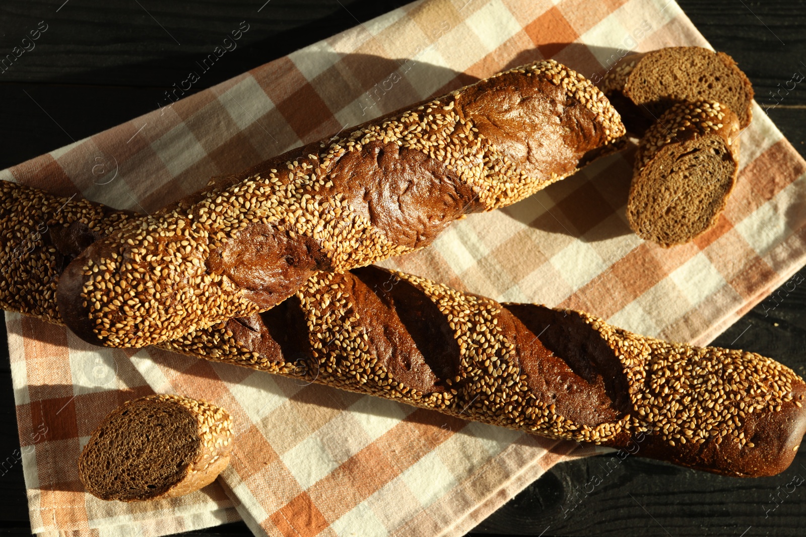 Photo of Fresh baguettes with sesame on black wooden table, flat lay