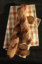 Photo of Fresh baguettes with sesame on black wooden table, flat lay