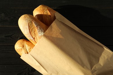 Photo of Fresh baguettes in paper bag on black wooden table, top view