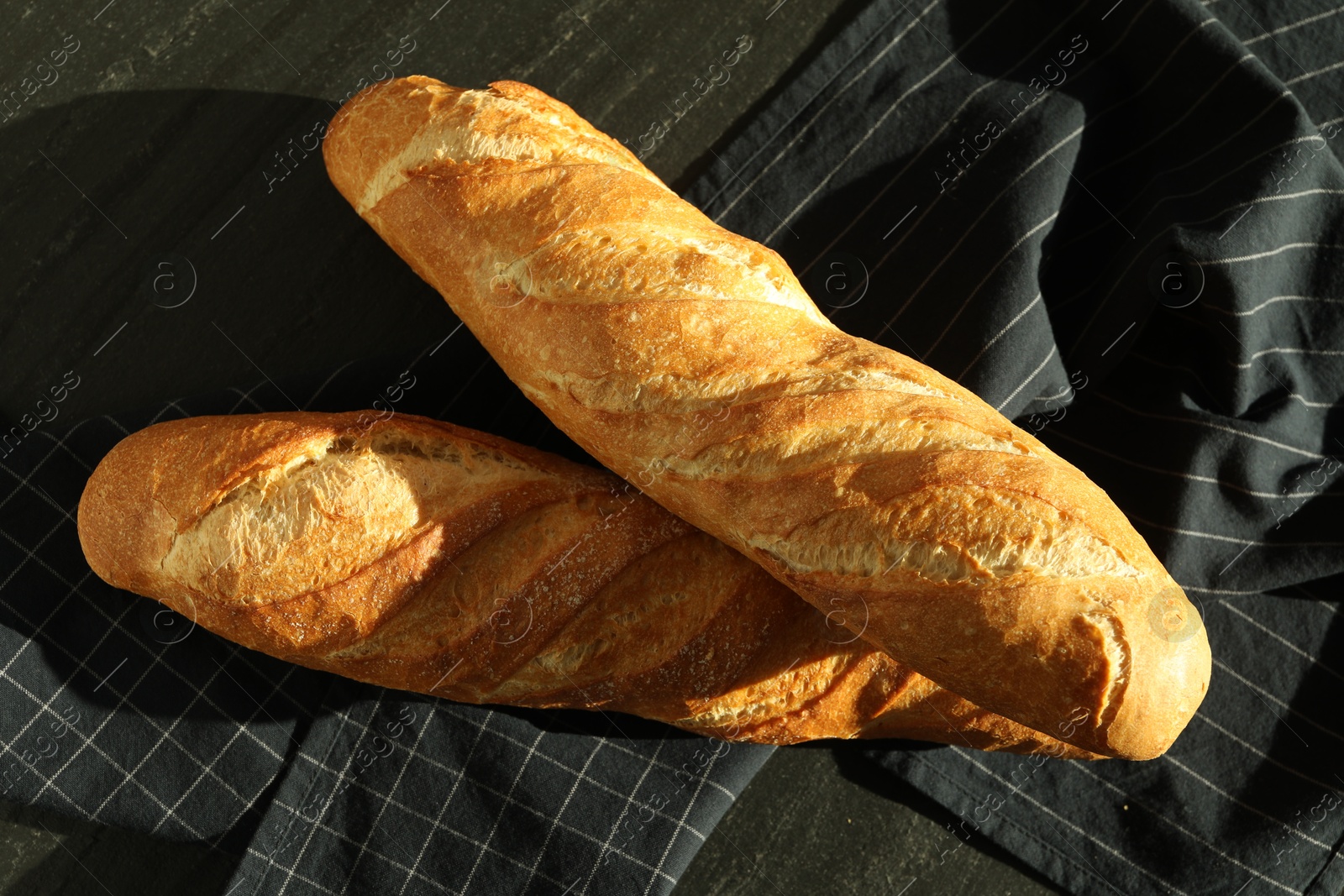 Photo of Freshly baked baguettes on black table, top view