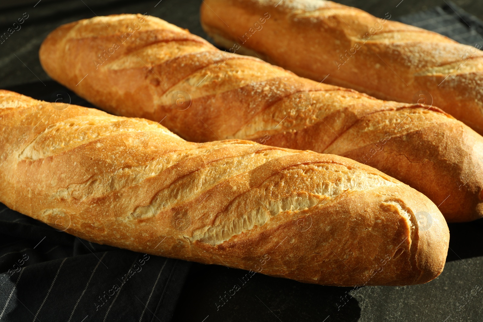 Photo of Freshly baked baguettes on black table, closeup