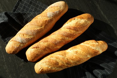 Photo of Freshly baked baguettes on black table, flat lay