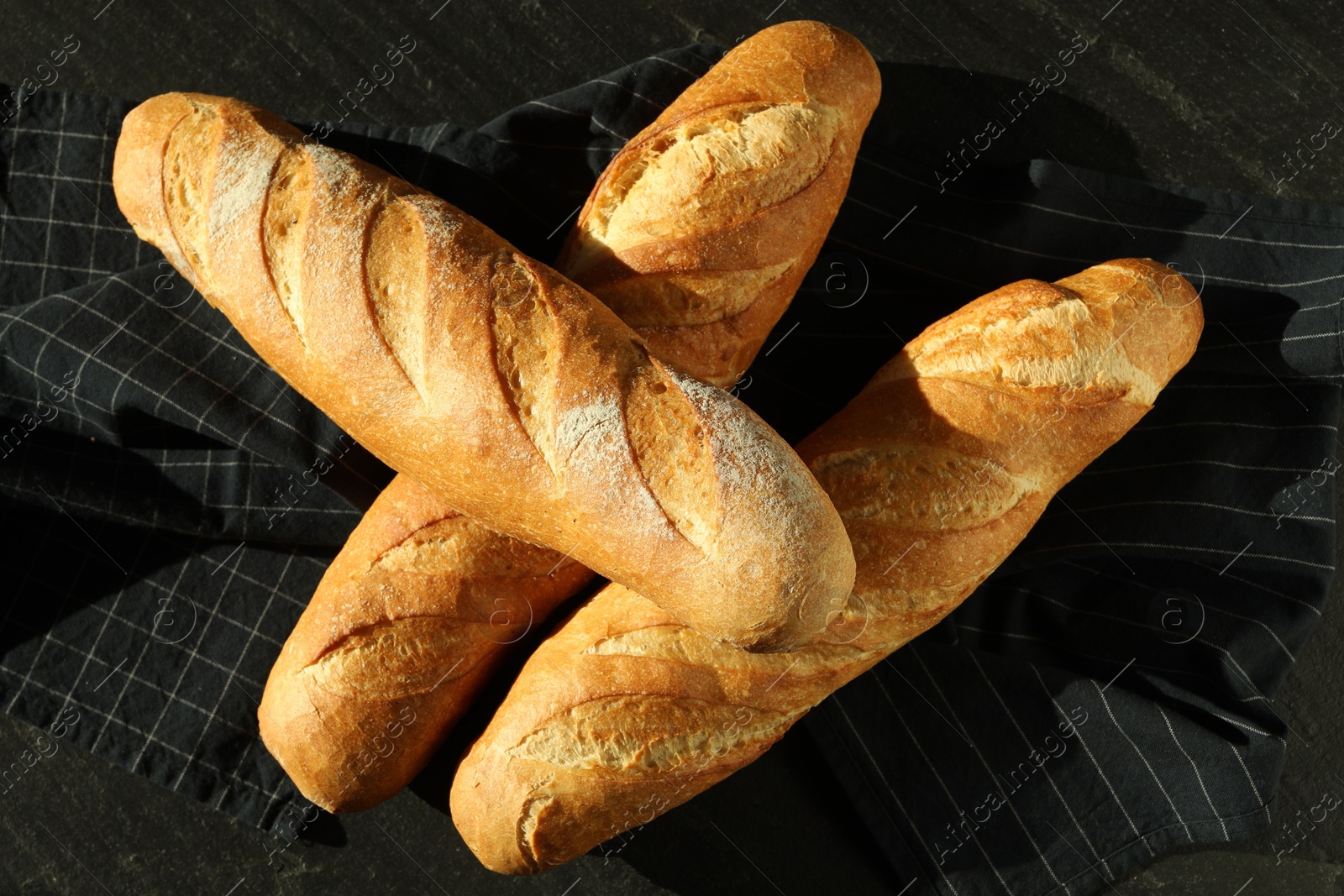 Photo of Freshly baked baguettes on black table, top view