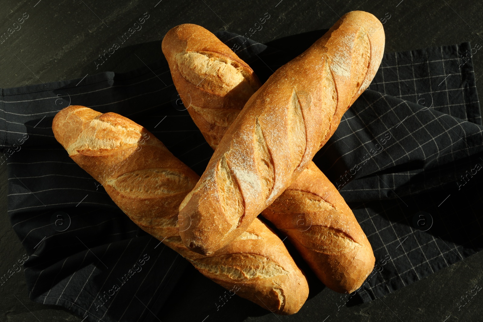 Photo of Freshly baked baguettes on black table, top view