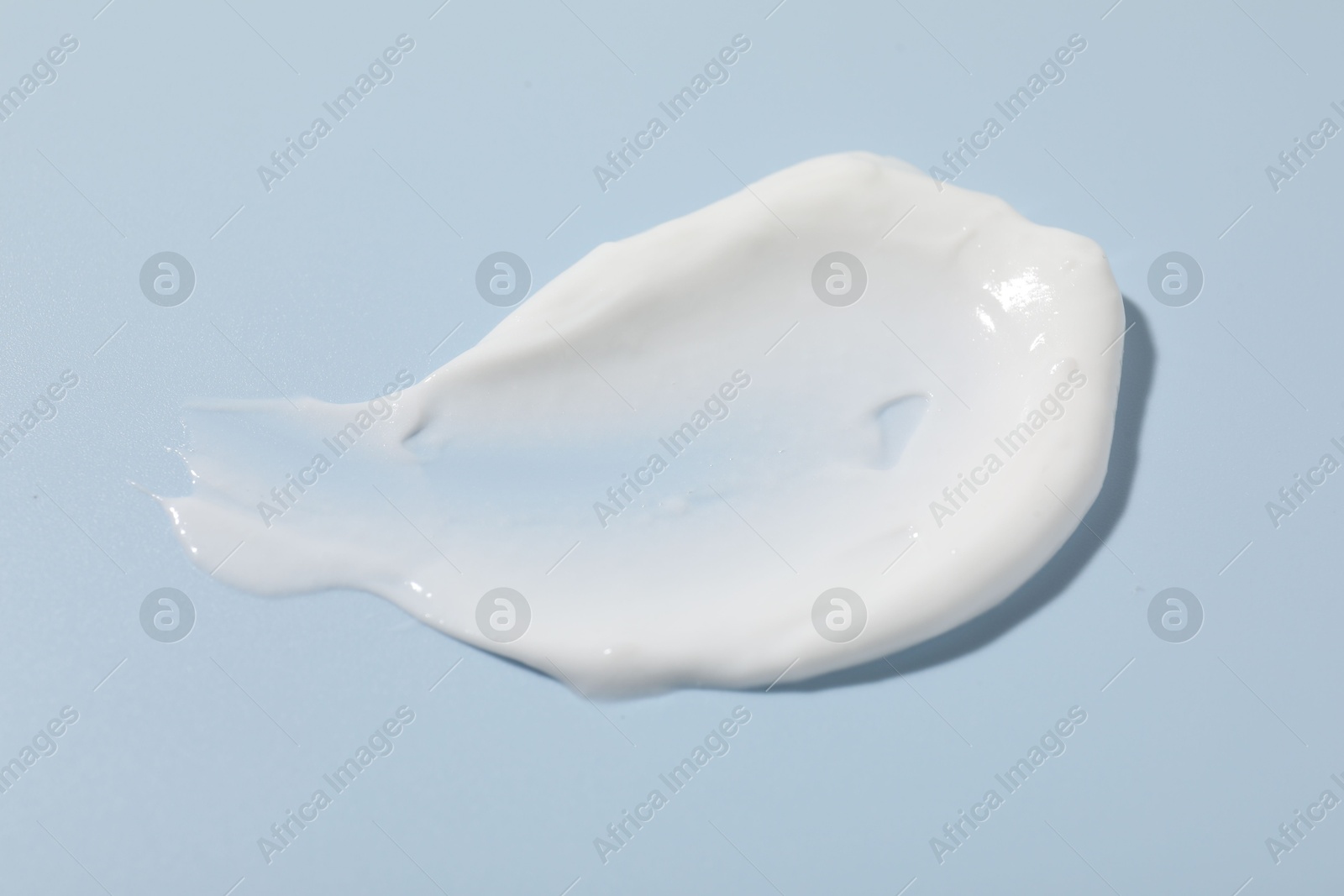 Photo of Sample of cream on light blue background, closeup. Cosmetic product